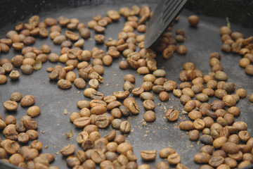 Green coffee beans roasting on the black pan