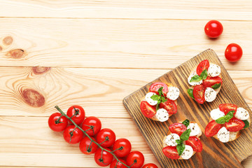 Bruschetta with mozzarella, tomatoes and basil leafs on wooden cutting board