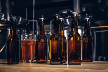 Bottles and glass of craft beer on wooden bar counter at the indie brewery.