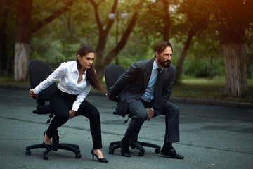 Man and woman sitting on office chairs outside. Looking aside. Ready to start.