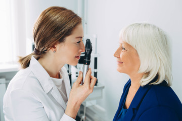 Doctor Optometrist examining senior woman's eye with ophthalmoscope
