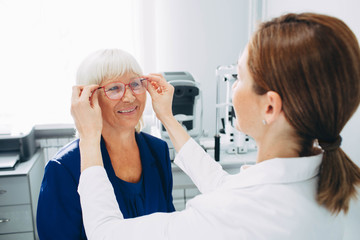 Happy senior woman trying out new reading glasses at optician office