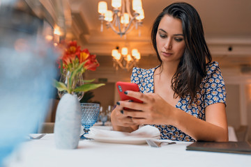Horizontal image of young business elegant woman wearing dress sitting in the restaurant using smartphone to do some notice for new project. Caucasian female working on mobile phone in cafeteria.