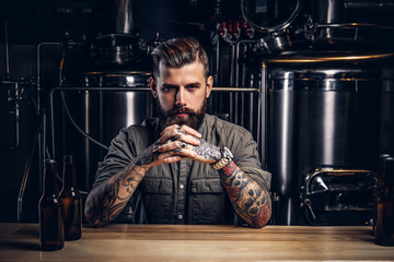 Portrait of a pensive tattooed hipster male with stylish beard and hair in the shirt in indie brewery.   - Powered by Adobe