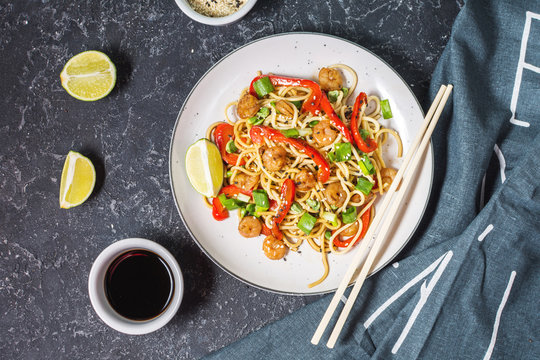Stir fry noodles with vegetables and shrimps on dark stone background.