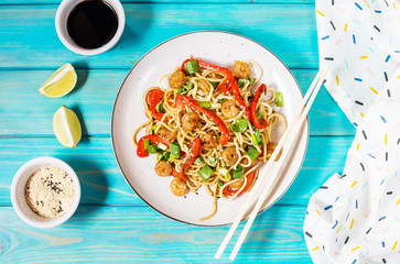 Stir fry noodles with vegetables and shrimps on blue wood background.