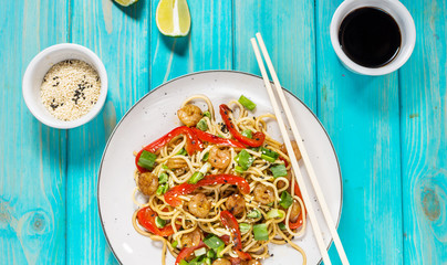 Stir fry noodles with vegetables and shrimps on blue wood background.