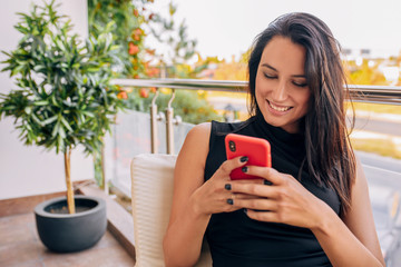 Happy brunette business woman reading news on smart phone indoor in a cafe. Smiling young female texting messages on mobile phone in the restaurant. Elegant lady shopping via free wireless on phone