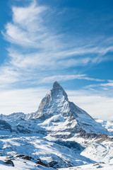 Scenic view on snowy Matterhorn peak in sunny day with blue sky and dramatic clouds in background, Switzerland