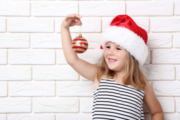 Little girl holding christmas bauble on brick wall background