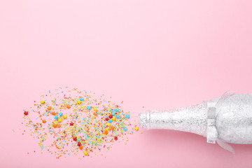 Champagne bottle with colorful sprinkles on pink background