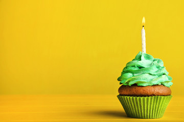 Tasty cupcake with candle on yellow background