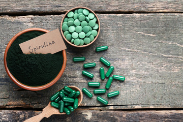 Spirulina powder and tablets on grey wooden table