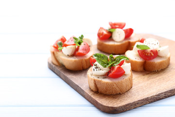 Bruschetta with mozzarella, tomatoes and basil leafs on wooden cutting board