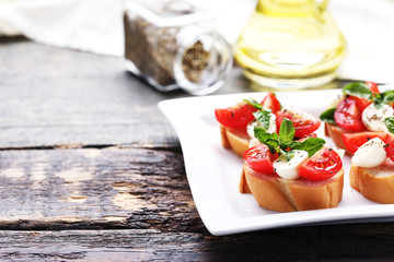 Bruschetta with mozzarella, tomatoes and basil leafs on grey wooden table