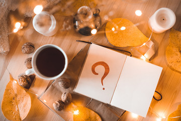 Cup of tea with opn notebook and question mark in it closeup. Top view. Autumn concept.