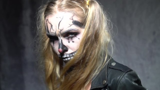 Closeup face of woman with creepy Halloween clown skull makeup looking into the camera. Creative, artistic, Halloween concept - video in slow motion