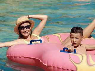 Young European lady and her son are enjoying their vacations. They are having fun in water park,...