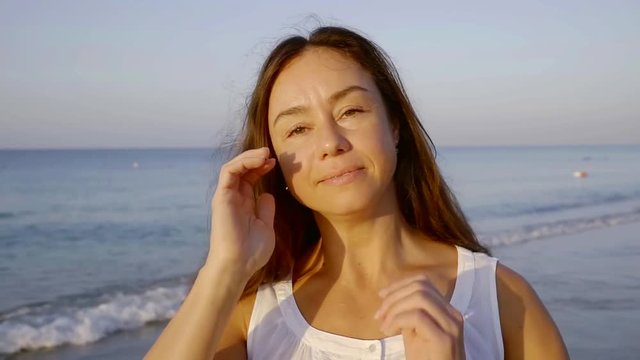 charming adult brunette woman is smiling and looking at camera, standing on ocean coast in summer