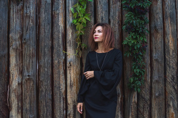 Portrait of a beautiful young woman in black dress on a background of old wooden wall