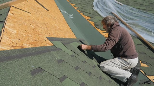 soft roof of shingles. Repair of the roof of a residential house. installation of soft tiles. partial replacement of the damaged roof. Dot repair. carpenter throws a hammer up and catches it. Worker