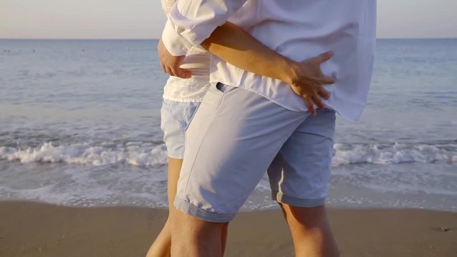woman is stroking ass of her beloved man, close-up, couple is standing on sea beach in morning