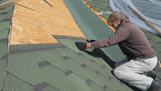 soft roof of shingles. Repair of the roof of a residential house. installation of soft tiles. partial replacement of the damaged roof. Dot repair. carpenter throws a hammer up and catches it. Worker