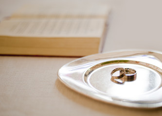 Eheringe drapiert auf einem silbernen Tablett neben einem Buch auf dem Altar / Wedding rings draped on a silver tray next to a book on the altar