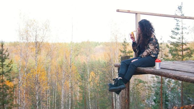 Curly woman sits on a altitude platform and eats banana.