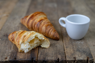 Tasty well-baked croissant on a wooden kitchen table. Light bread prepared for breakfast.