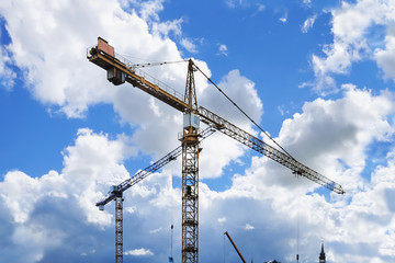 Construction tower cranes against a partly cloudy bright blue sky
