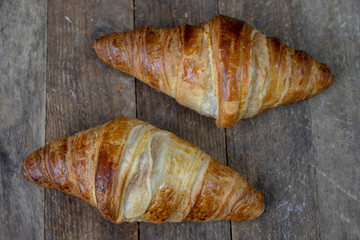 Tasty well-baked croissant on a wooden kitchen table. Light bread prepared for breakfast.