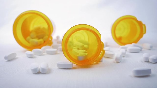 Prescription pills fall in a slow motion on three orange pharmaceutical bottles. Capsules represent the opioid crisis in America, narcotic addiction, overdoses and repealing the affordable care act.