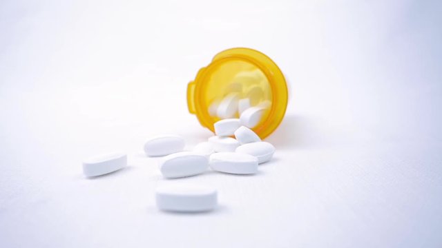Prescription pill bottle dropping and falling over in slow motion. The capsules represent the opioid crisis in America, narcotic addiction, overdoses, substance abuse and repeal of the affordable act.