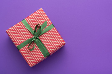 Wrapped gift box with colored ribbon as a present for Christmas, new year, mother's day, anniversary, birthday, party,  on violet background, top view. Present for a colleague at work.