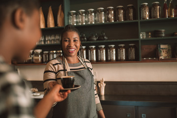 Smiling young African barista giving her customer a cappuccino