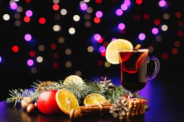 Fototapeta na wymiar New Year and Christmas decor. Glasses with mulled wine stand on table with oranges, apples, cinnamon and other species in the dark room with festive decor
