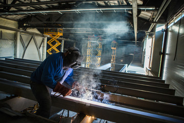 welder builder sitting on a metal beam welding at height