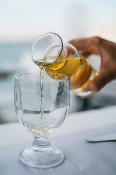 A woman's hand with a bottle of white wine pouring wine into a glass