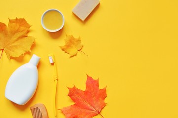 Flat lay organic bath products. Photo natural shampoo, toothbrush, wooden comb, homemade soap, honey and orange maple leaves on a yellow background. Autumn personal care