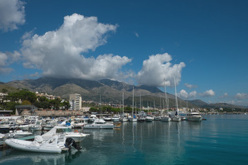 Fototapeta na wymiar Boats and yachts in the harbor in Formia, with mountains and clouds in the background.