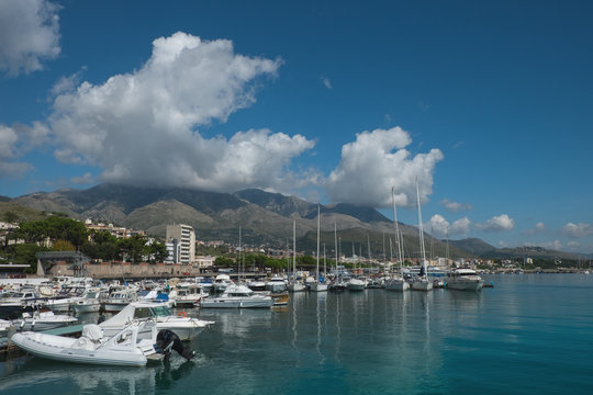 Boats and yachts in the harbor in Formia, with mountains and clouds in the background.