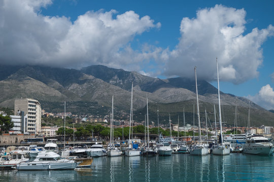 Boats and yachts in the harbor in Formia, with mountains and clouds in the background. 