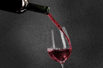 Red wine pouring into glass on background