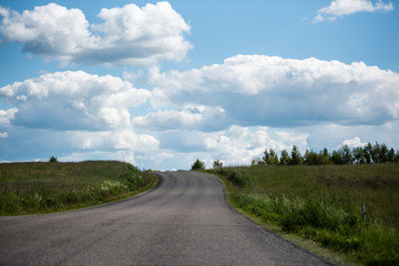 Rural landscape with green field, road and cumulus clouds in summer