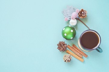 Flat lay Christmas composition. Cup of coffee, green ball, pine cones and cinnamon sticks on a blue background. Happy New Year greeting card