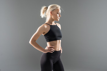 Close up of fit woman's torso with her hands on hips. Female with perfect abdomen muscles on grey background with copyspace.