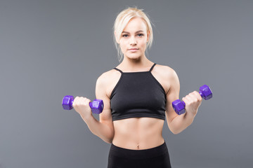 portrait of pretty sporty woman holding weights isolated on gray background