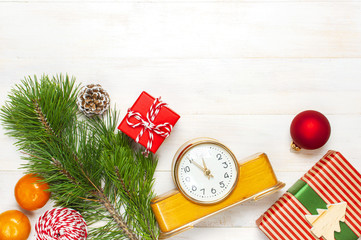 Fototapeta na wymiar New Year or Christmas background. Retro alarm clock pine branches cones gifts presents toys red ball on white wooden background top view with copy space. Christmas timer Time to celebrate Xmas