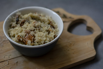Bowl of wild mushroom Risotto on a wooden board with grey background. Shallow depth of field.